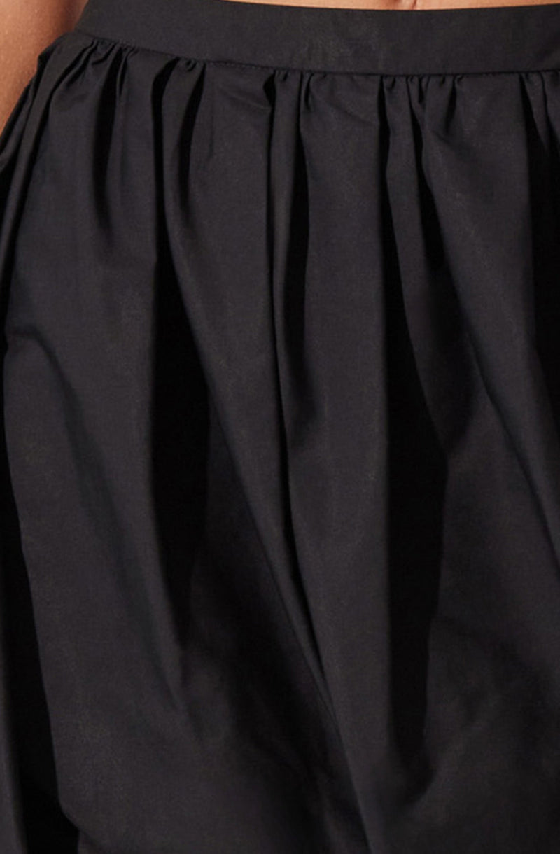 A close-up of a black skirt made from a shiny, smooth fabric. The skirt features a fitted waistband and gathers or pleats starting from the waistband, creating a voluminous, flowing appearance.