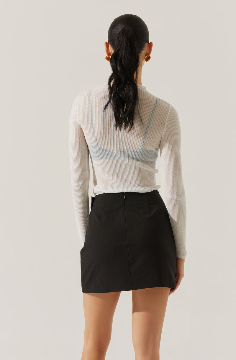The person is wearing a long-sleeved, ribbed knit sweater in a light, neutral color with subtle vertical stripe details. The sweater appears to be fitted and slightly sheer. They are also wearing a high-waisted black mini skirt with a front zipper and a smooth finish.