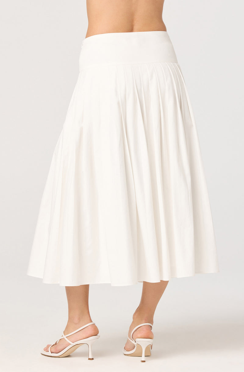 A person is wearing a high-waisted, full-length white skirt with pleats. The skirt has a smooth waistband and falls to mid-calf length. The individual is also wearing white high-heeled sandals with thin straps.