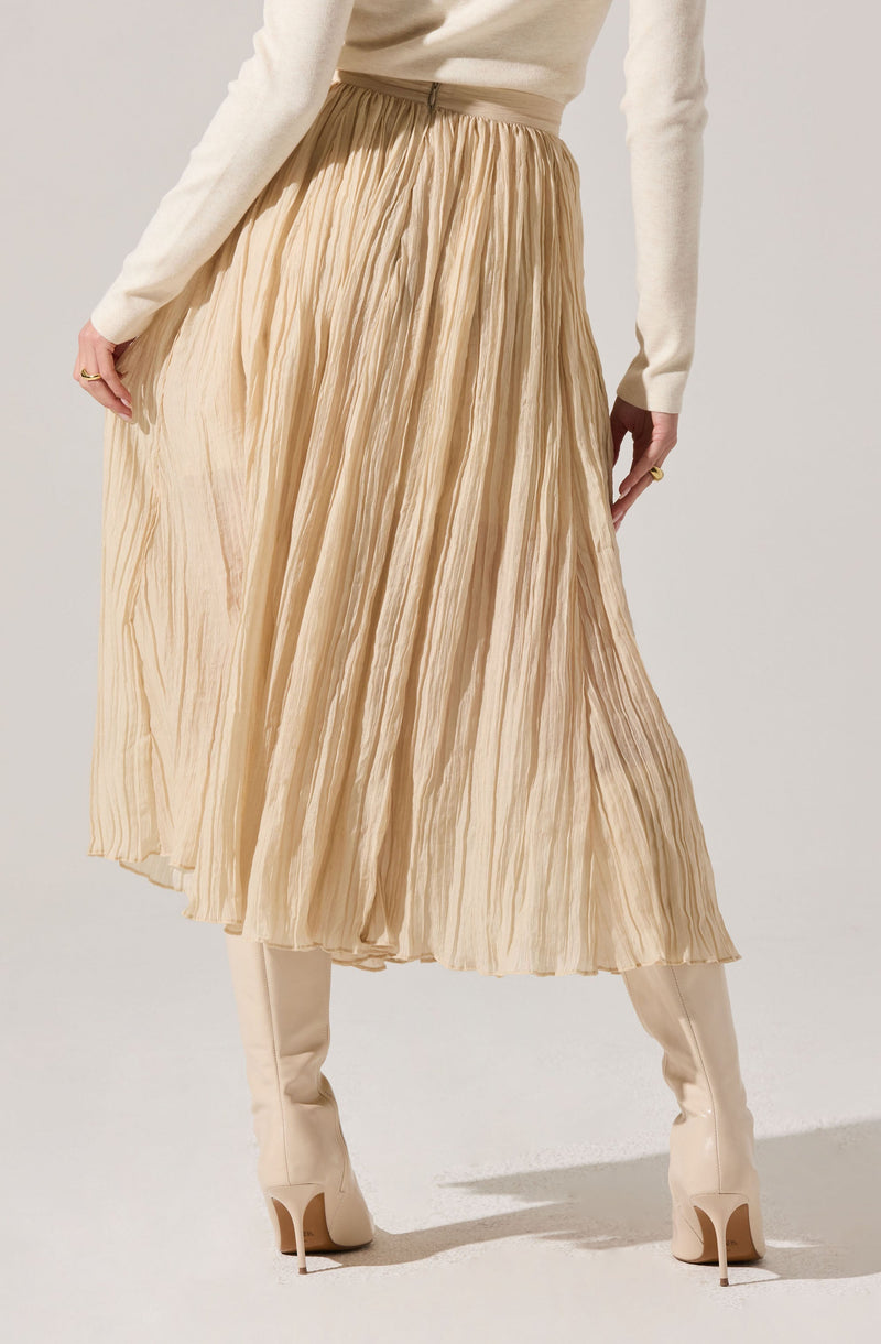 A woman is wearing a long, pleated, beige skirt with a high waist. She has paired it with knee-high, off-white boots with high heels. She is also wearing a long-sleeved, cream-colored top.