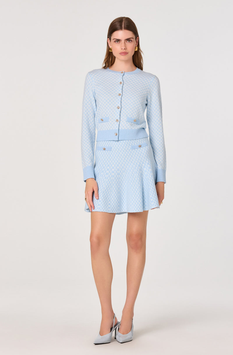 Woman in light blue patterned jacket and matching skirt, wearing gray high heels.