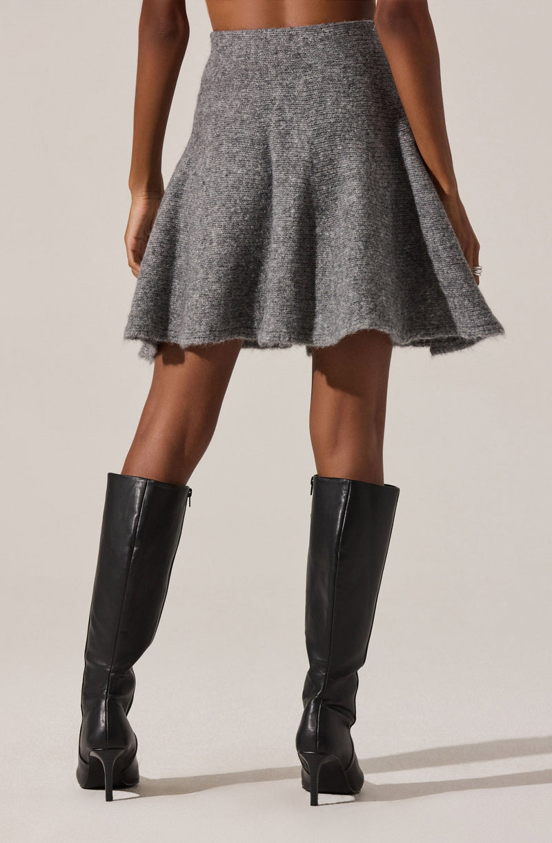 A woman is wearing a high-waisted, gray, textured wool skirt with a flared silhouette. She pairs it with black, knee-high, heeled leather boots.