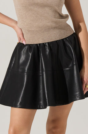 A person is wearing a beige knit sleeveless top with a fitted waistband and a black, shiny, faux leather A-line skirt with an elastic waistband.