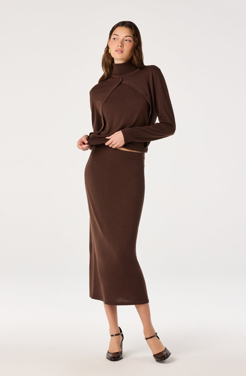 Woman in a brown long skirt and matching brown sweater with a high neckline and button details.