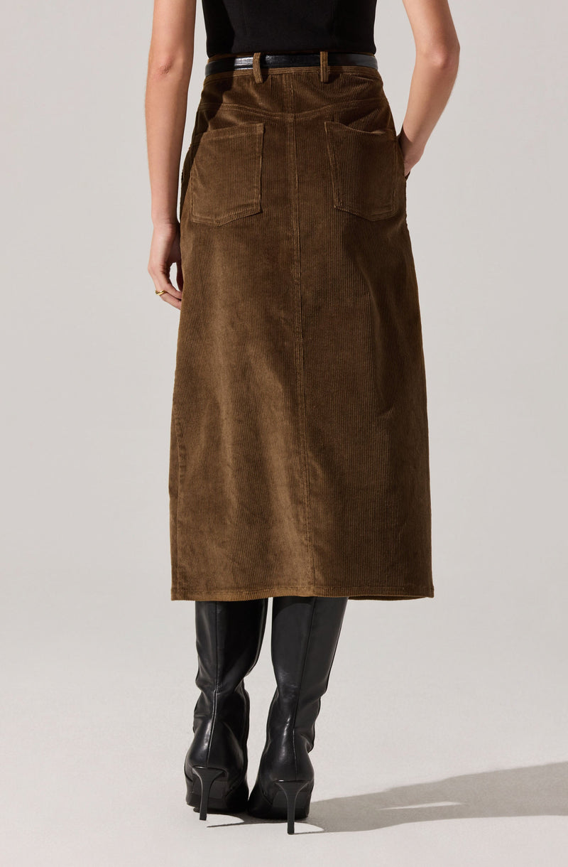 A person is wearing a high-waisted, long brown corduroy skirt with large back patch pockets. They have paired it with knee-high black leather boots with pointed toes and stiletto heels, and a black top tucked into the skirt.