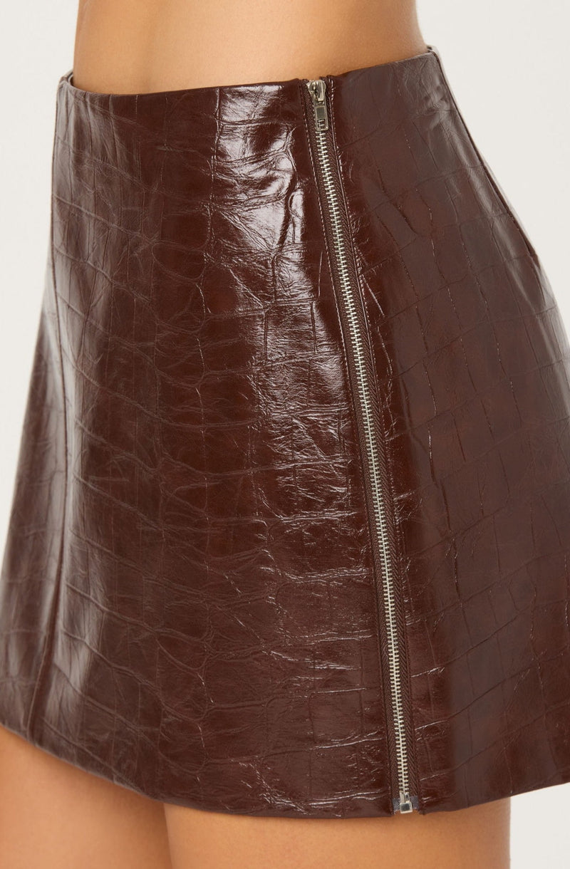 A close-up of a high-waisted, dark brown leather skirt with a shiny, crocodile-embossed texture. The skirt features a visible front zipper with a silver pull running vertically down the center.