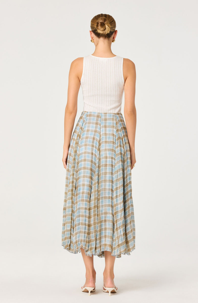 Woman wearing a sleeveless white knit top and a long, plaid beige and blue skirt.