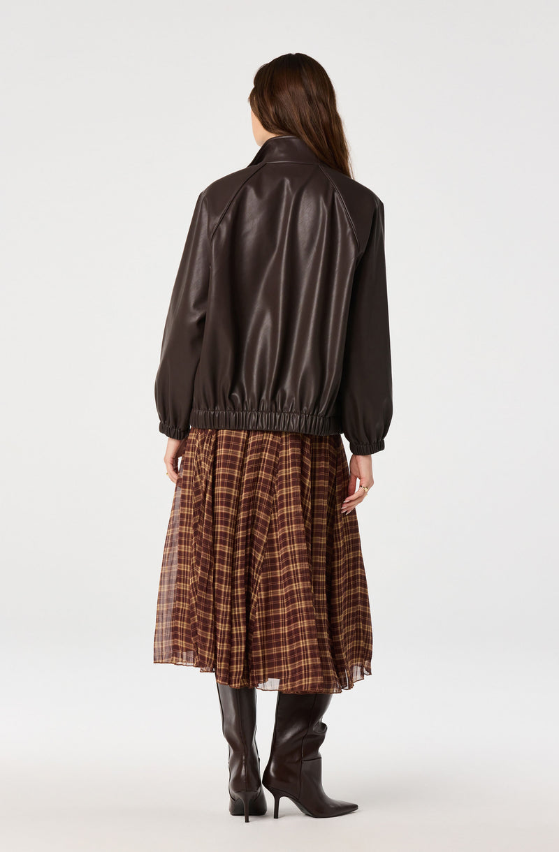 Woman wearing a dark brown leather jacket and a plaid brown skirt with black high-heeled boots.