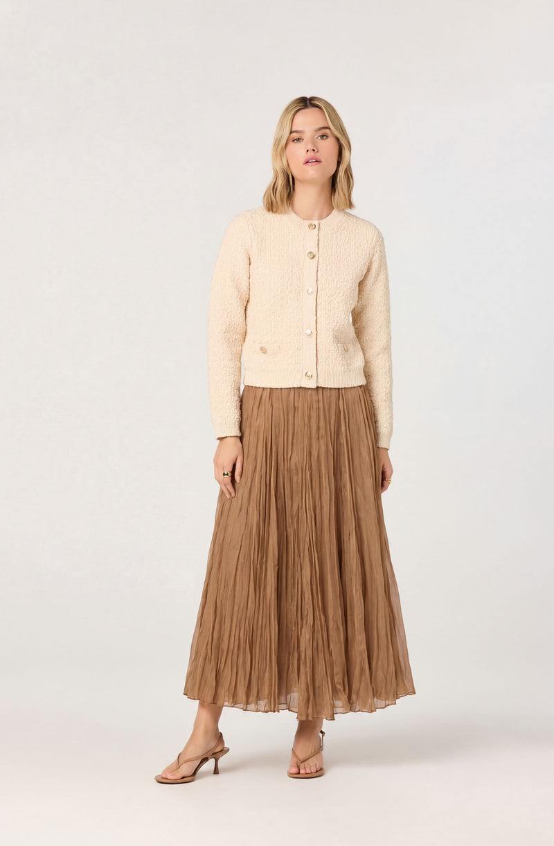 Cream textured cardigan with buttons and a long, pleated tan skirt.