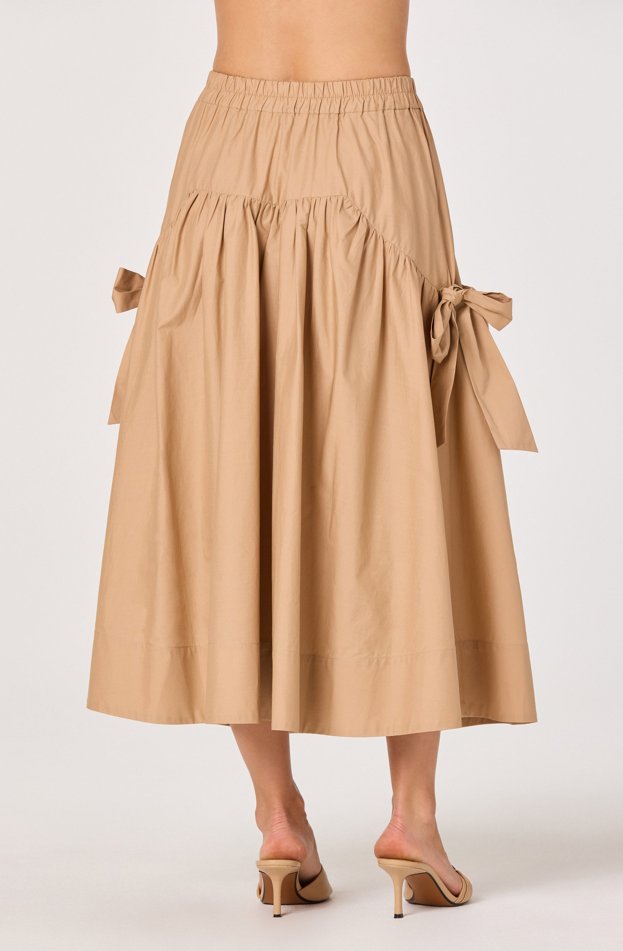 Beige midi skirt with bows on sides and elastic waistband, paired with beige heels.