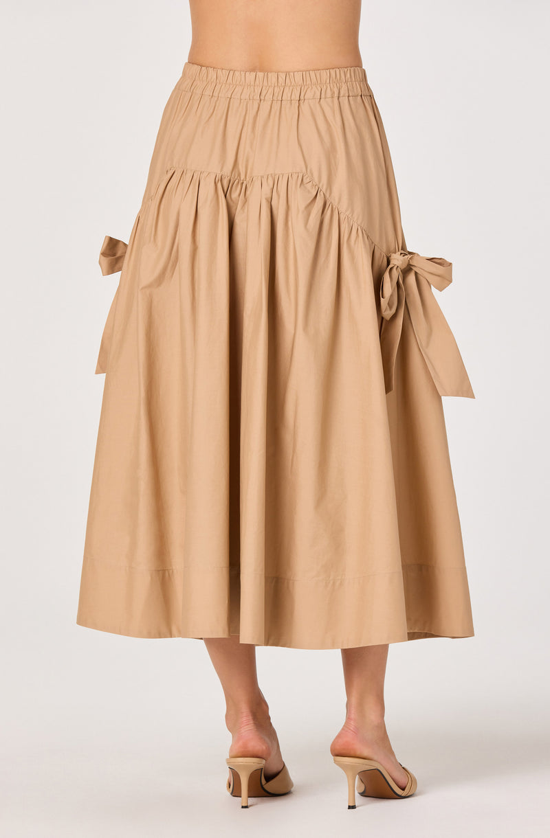Beige midi skirt with bows on sides and elastic waistband, paired with beige heels.