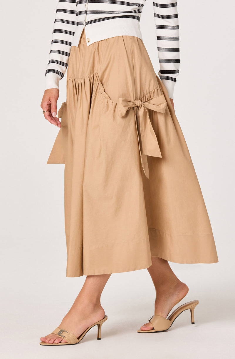 Beige wide-leg midi skirt with a front bow tie detail, paired with neutral heels and a striped top.