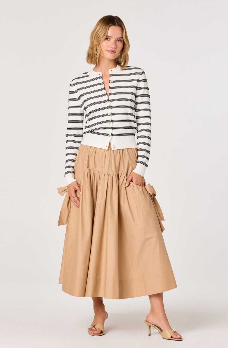 Woman wearing a white and gray striped long-sleeve cardigan with beige wide-leg skirt and beige high heels.