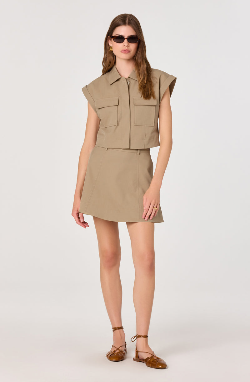 Woman wearing a beige sleeveless shirt with flap pockets and a matching beige skirt.