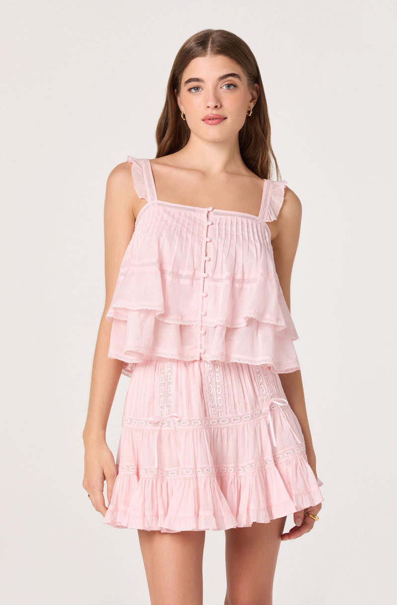 Girl in pink sleeveless ruffled top and matching skirt with embroidery details.