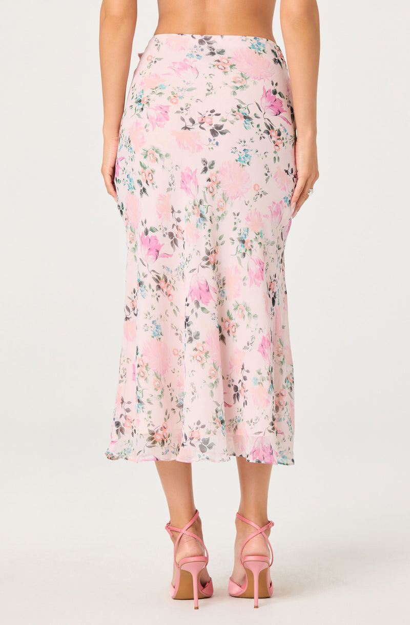 A woman wearing a flowy, high-waisted, floral midi skirt with pink, gray, and blue flowers.