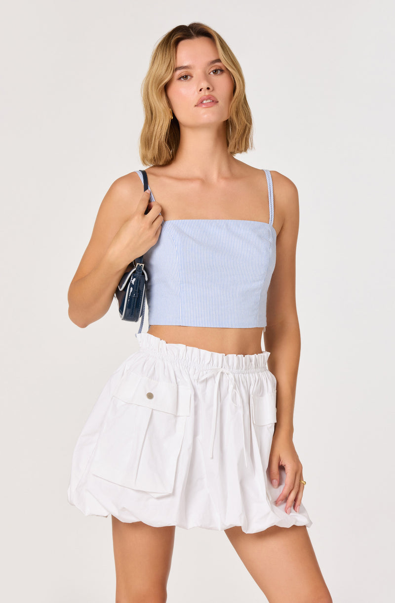 Woman in a light blue striped crop top with thin straps and white puffy shorts with large pockets.