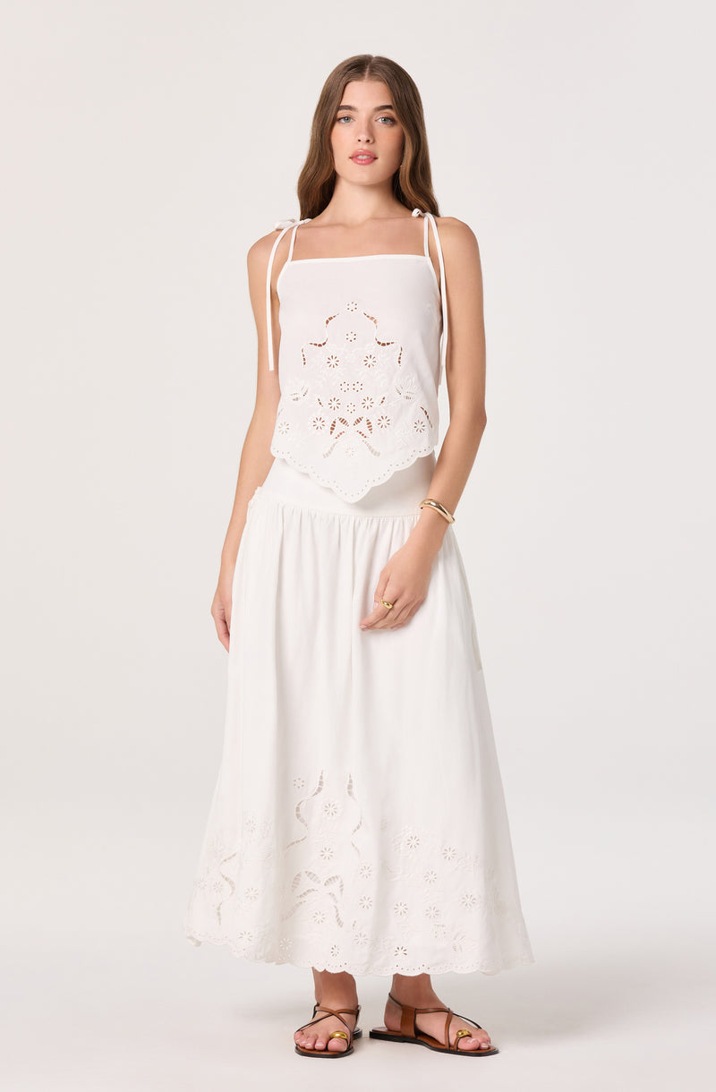 White sleeveless top with embroidered eyelet details and tie straps, paired with a long, white eyelet maxi skirt.