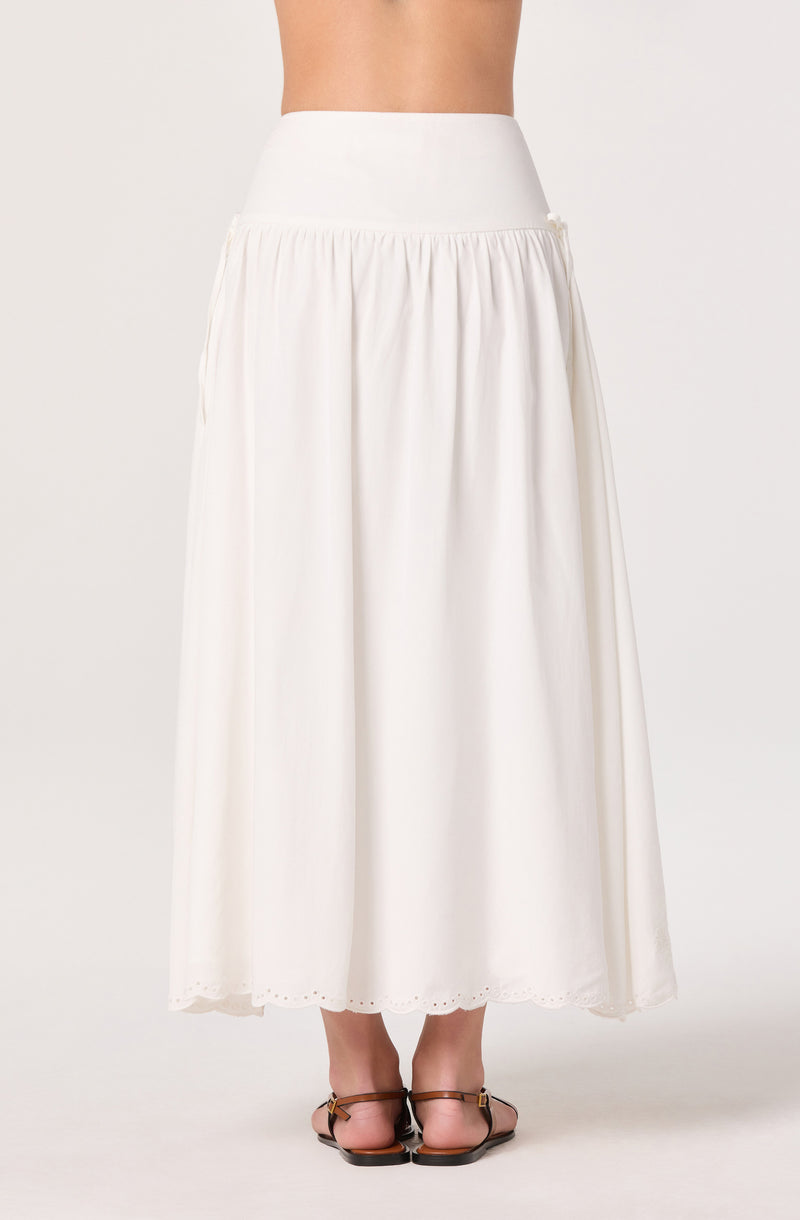 Long white skirt with a high waistband and eyelet hem, paired with brown sandals.