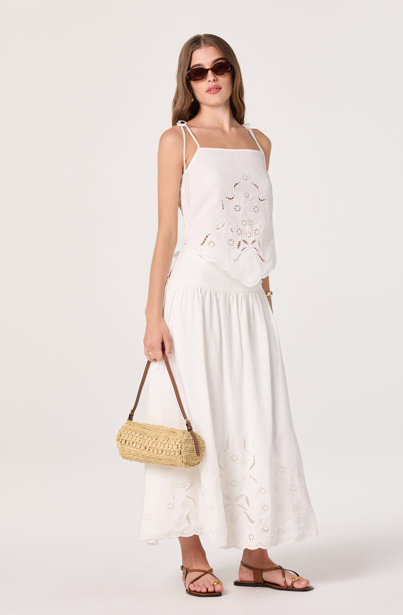 Woman wearing a white sleeveless top with eyelet details and a white maxi skirt with eyelet embroidery.
