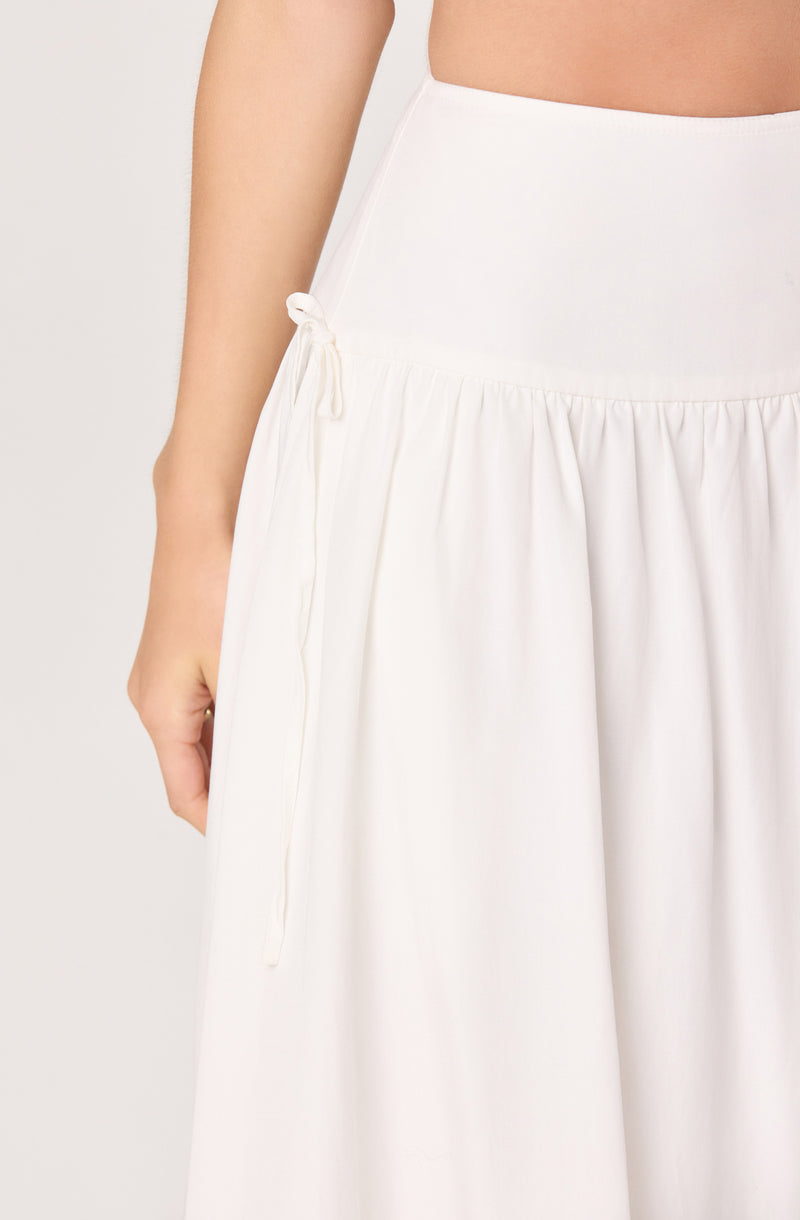 White skirt with a side tie and pleated detail at the waist.