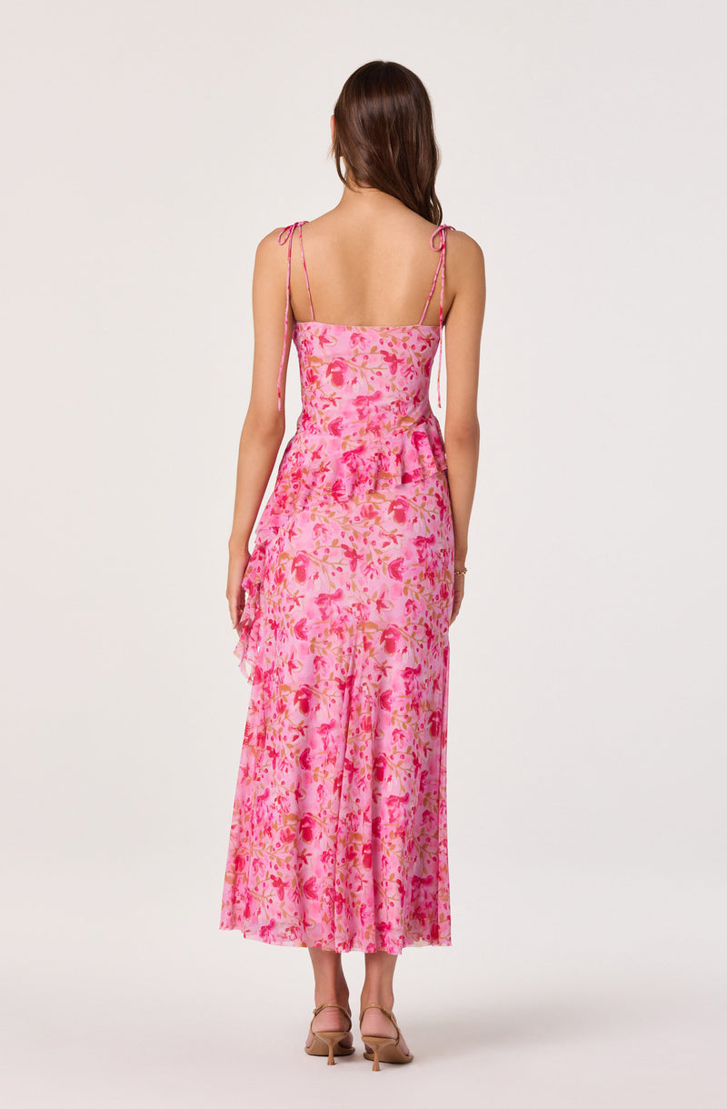 Back view of a woman in a pink floral sleeveless dress with spaghetti straps and a ruffled hem.