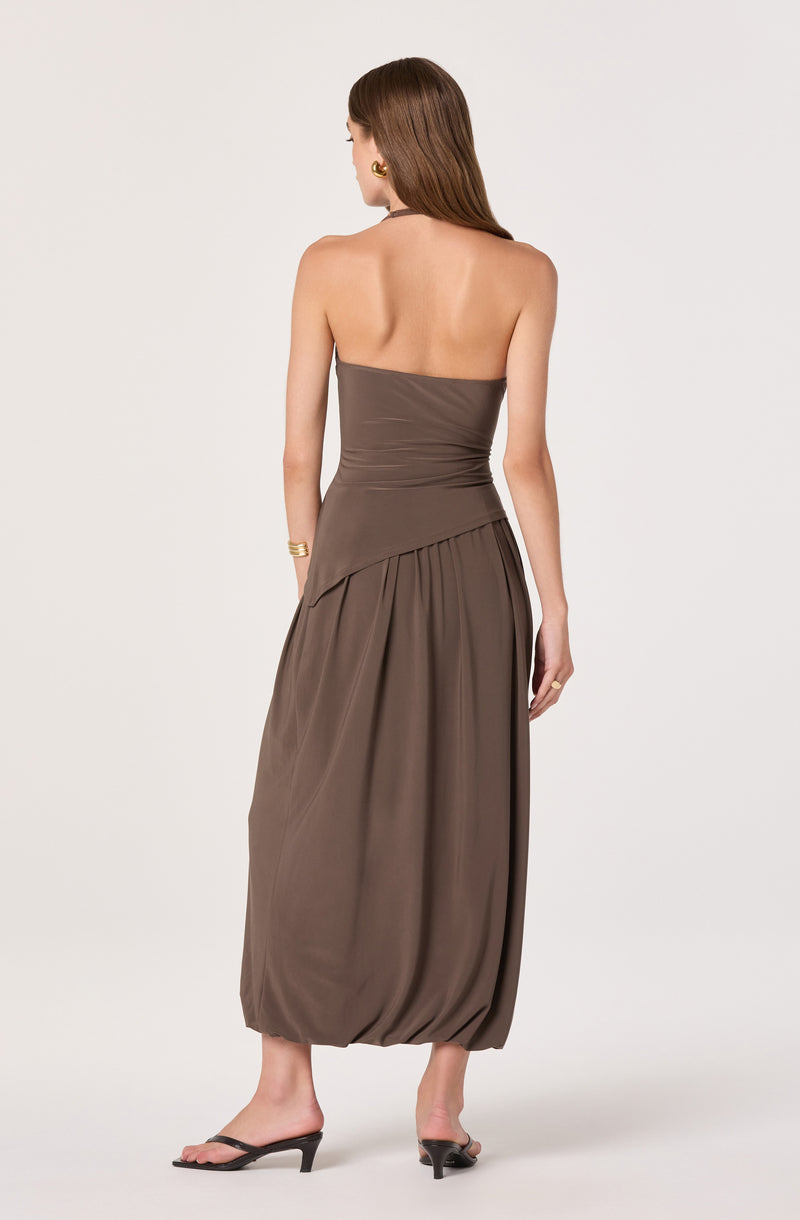Back view of a woman in a strapless taupe maxi dress with pleated and draped details.