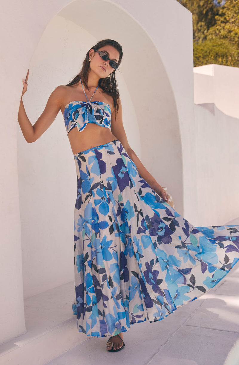 Woman wearing a blue floral strapless top and matching long, flowing skirt.