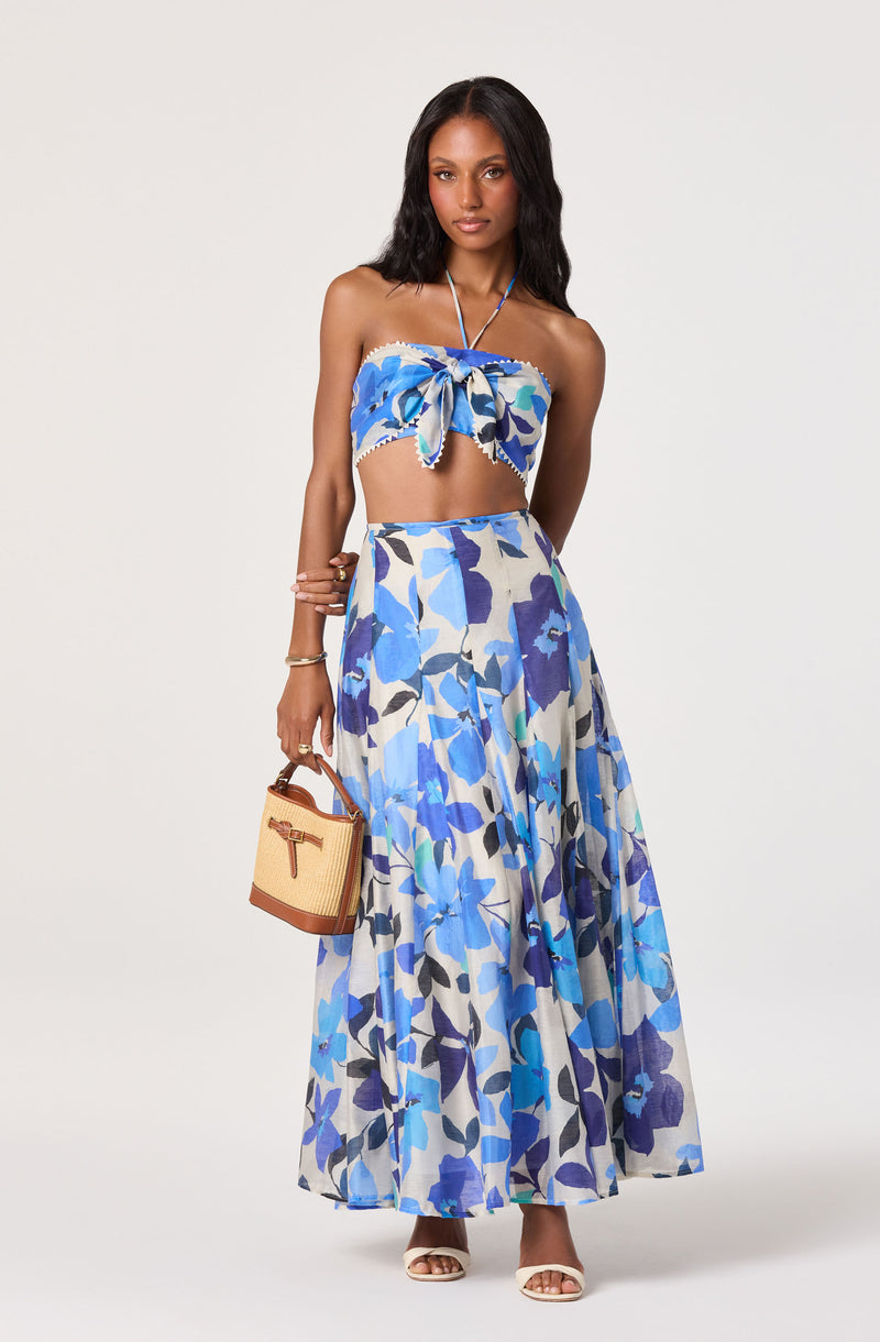 Woman wearing a blue floral strapless crop top and matching long skirt, holding a wicker bag.