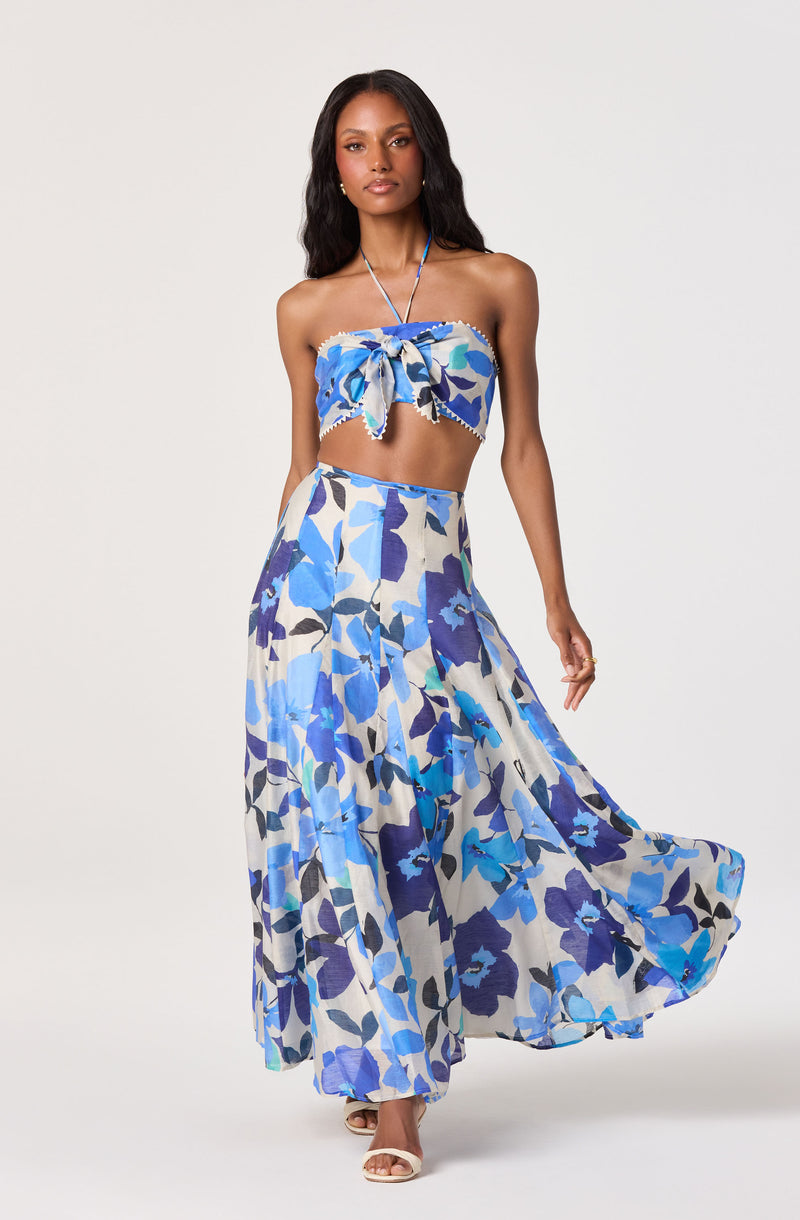 Woman wearing a blue floral strapless crop top with bow, matching high-waisted flowy skirt.