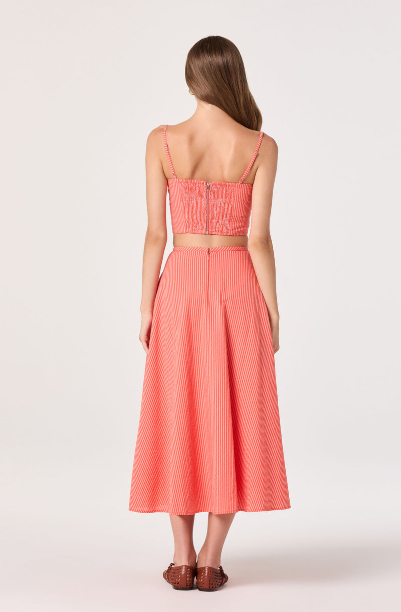 Woman wearing a coral and white striped crop top with spaghetti straps and a matching high-waisted A-line skirt.