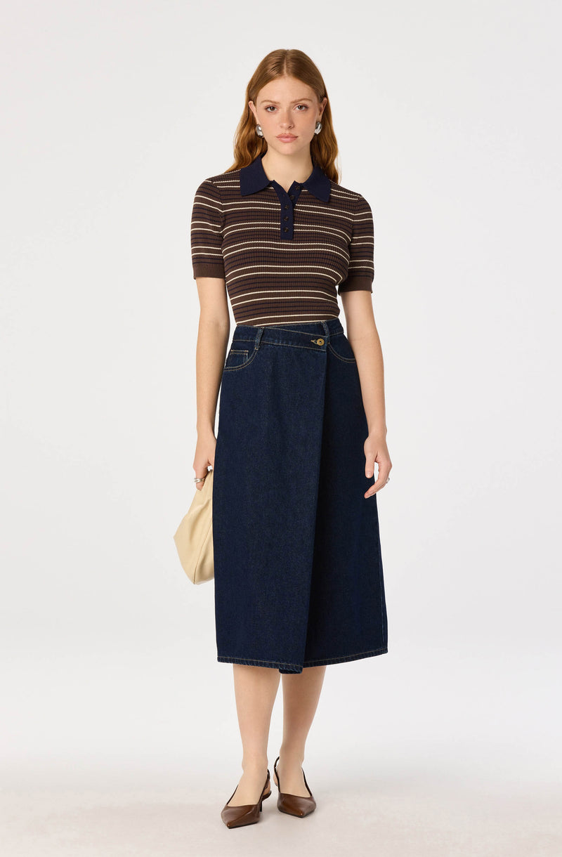 Woman wearing a striped brown and navy polo shirt with a dark collar, wide-leg denim skirt, brown shoes, and holding a beige bag.