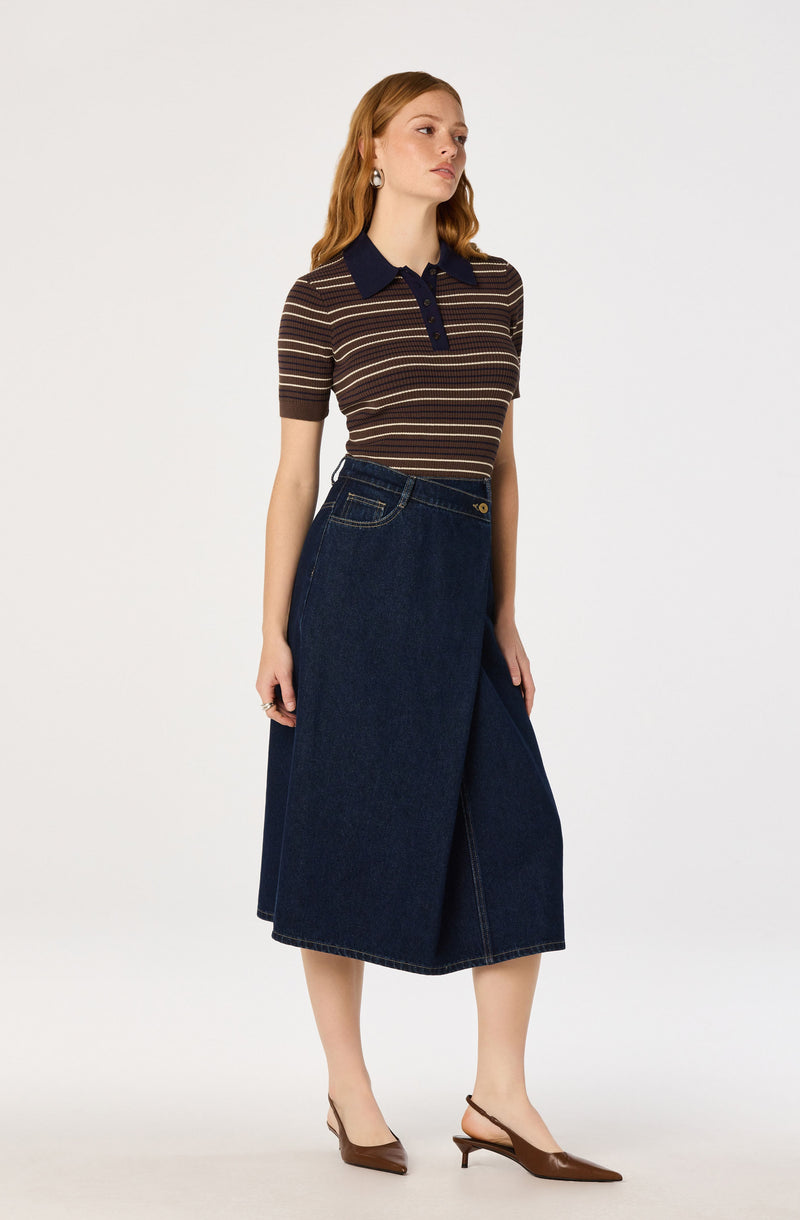 Woman wearing a striped brown and beige top with a navy collar and buttons, a dark denim skirt, and pointed brown heels.
