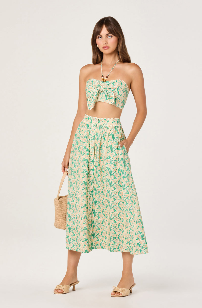Woman in a strapless, patterned crop top and wide-leg matching pants, holding a straw bag.