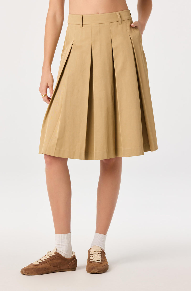 Beige pleated midi skirt with a high waist and front pleats, paired with brown sneakers and white socks.