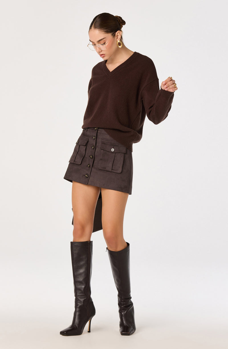 Woman in a brown V-neck sweater, dark gray button-front mini skirt, and black knee-high boots.