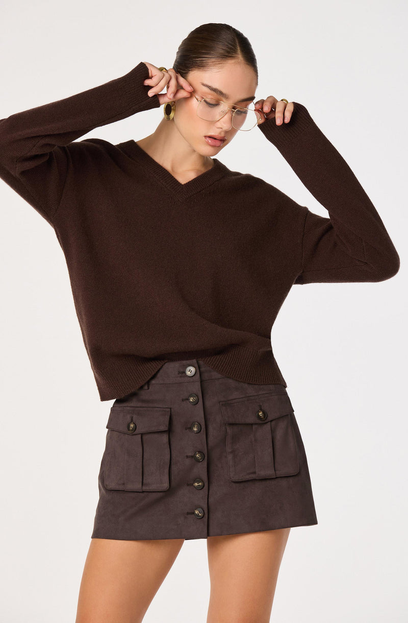 Woman wearing a dark brown V-neck sweater and a high-waisted, button-front skirt with large pockets.