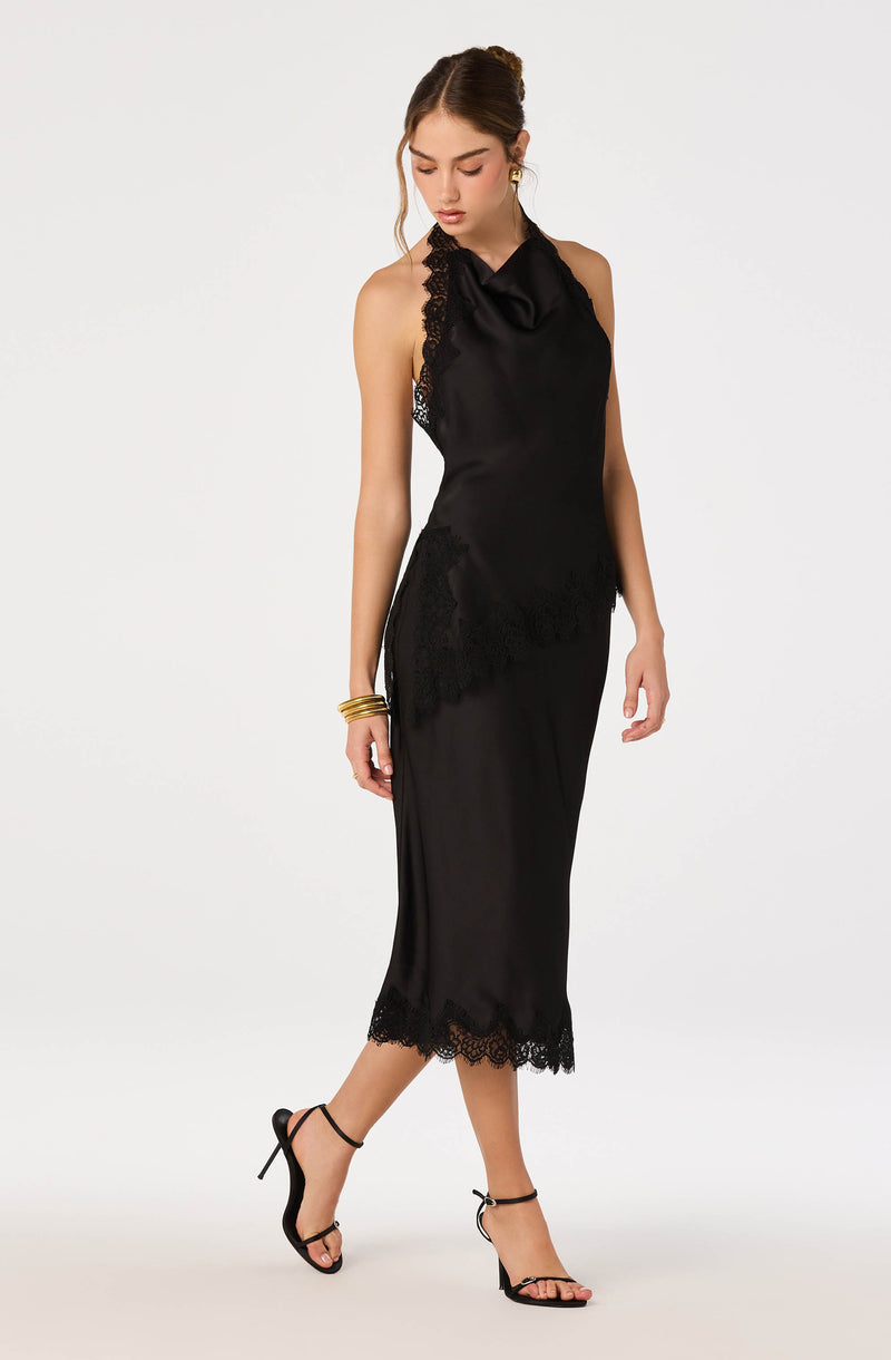 Woman wearing a black satin dress with lace details and a high neckline, paired with black strappy heels.