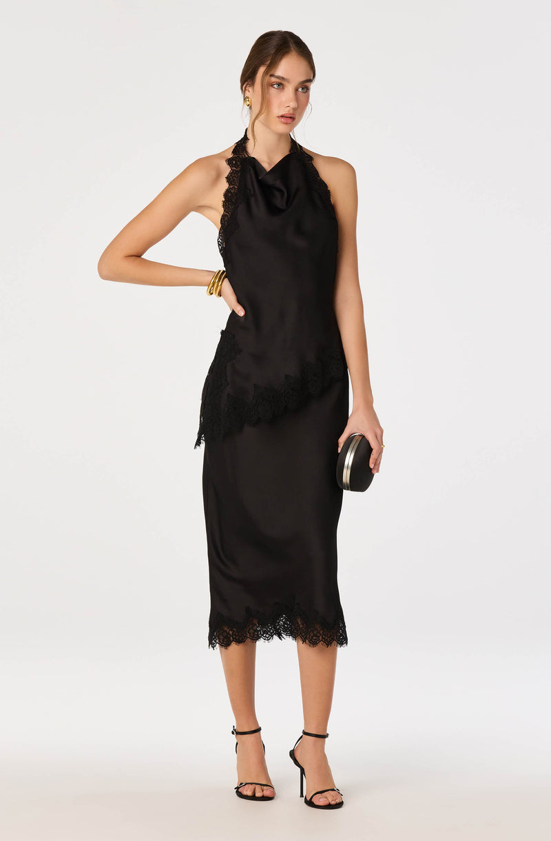 Woman wearing a black satin slip dress with lace trim, and black high heels, holding a round clutch.
