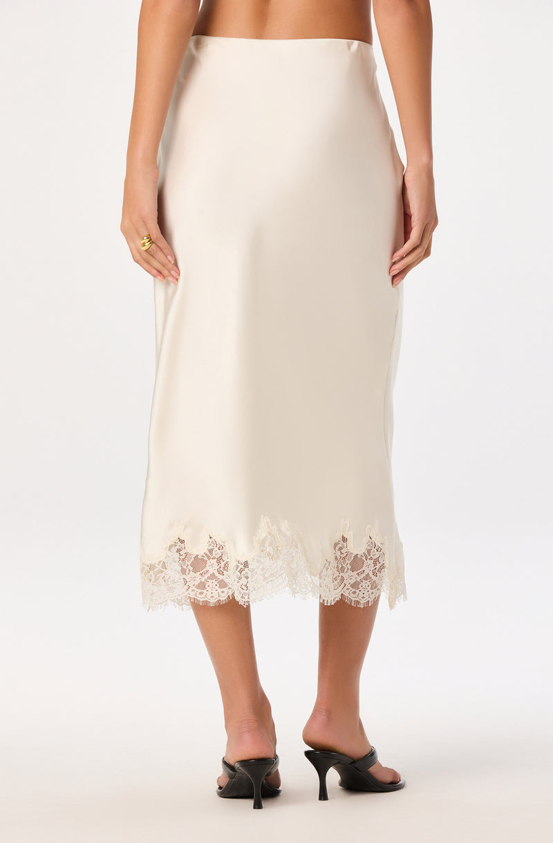Cream-colored skirt with lace trim at the hem, midi length, worn with black heels.