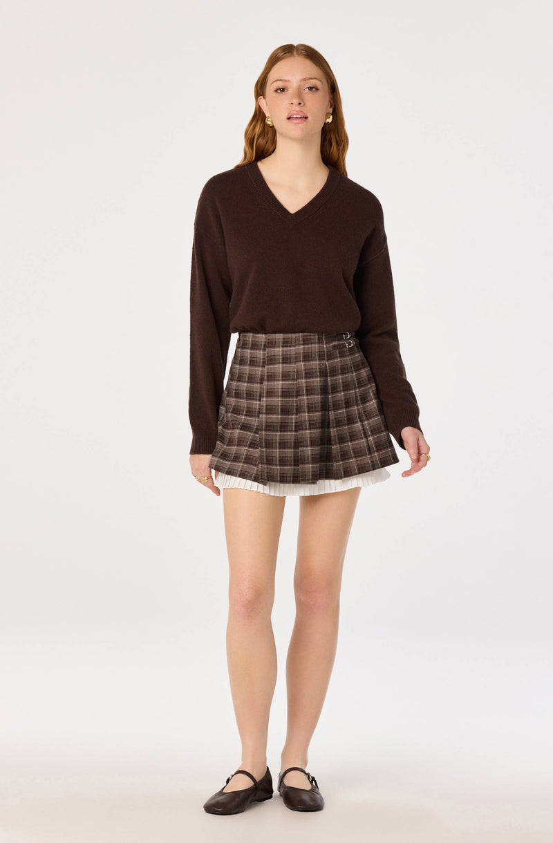 Woman wearing a dark brown V-neck sweater, plaid skirt with pleats, and brown shoes.