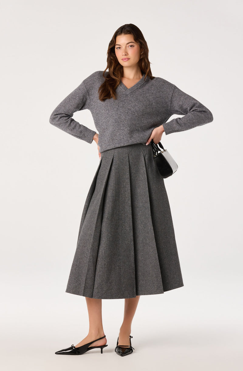 Woman wearing a grey cropped sweater and a pleated grey midi skirt.