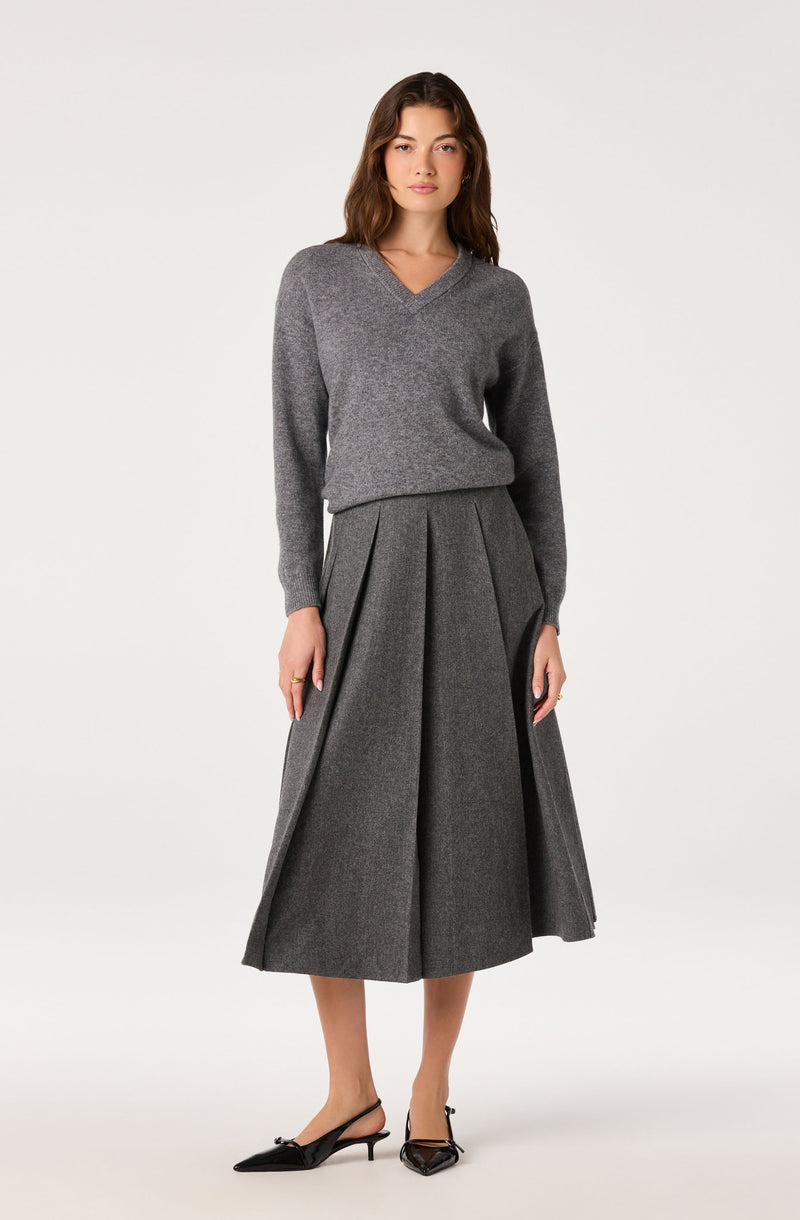 Woman wearing a gray V-neck sweater and a high-waisted gray pleated midi skirt with front pleats.