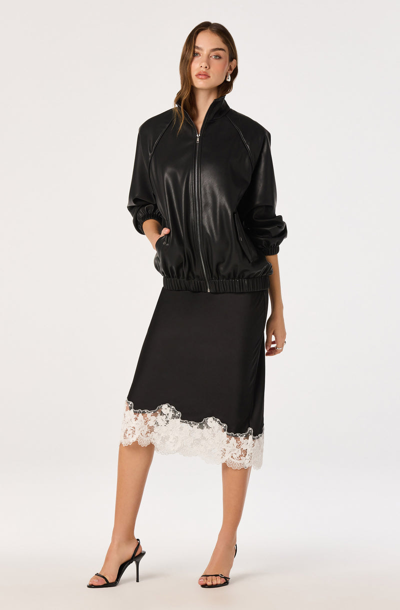 Woman in a black leather jacket, black dress with white lace hem, and black high heels.