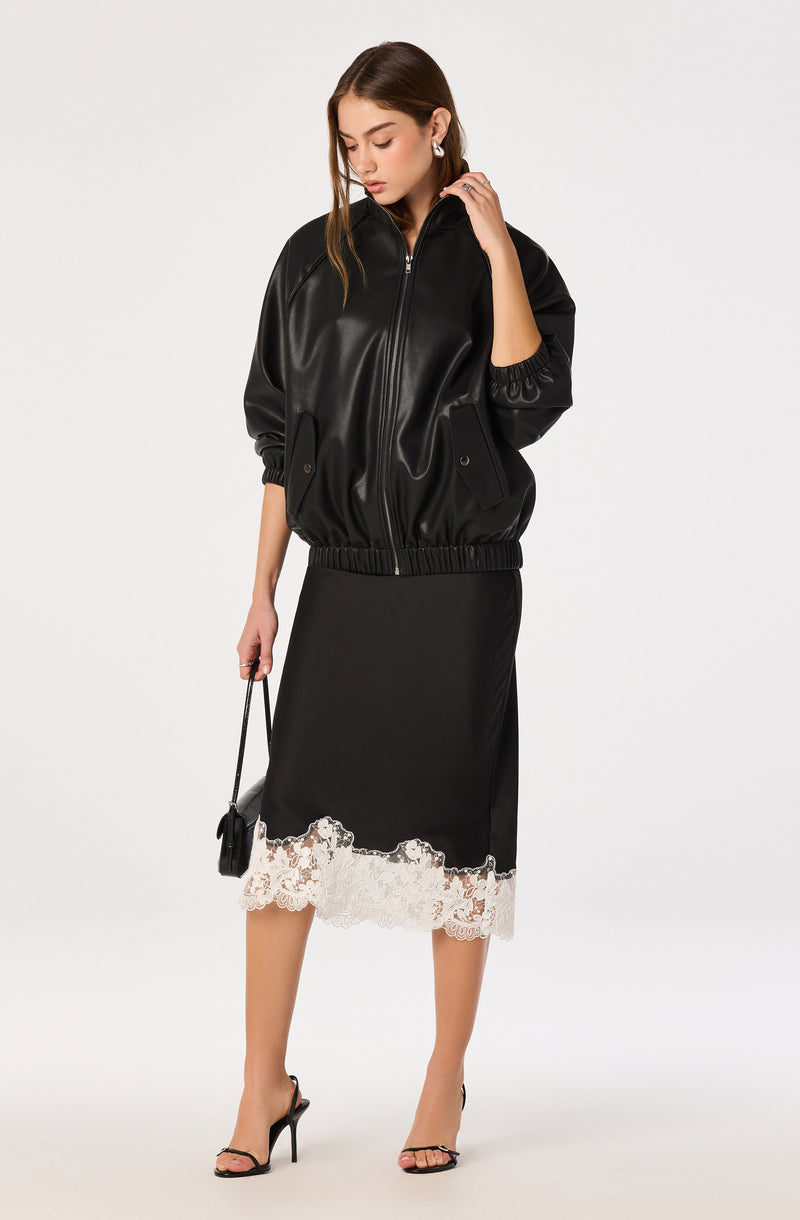 Woman in black leather jacket, black skirt with white lace hem, and black high-heeled sandals.