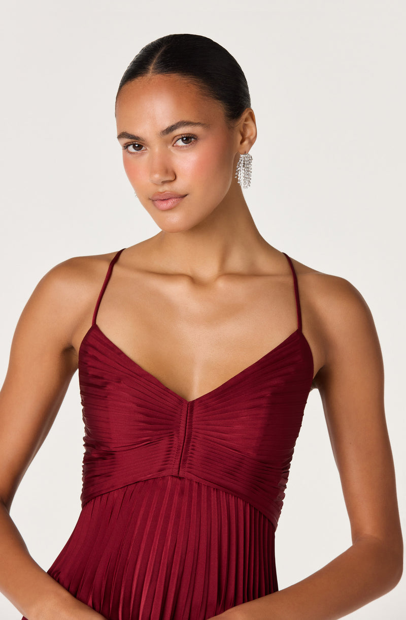 Woman in a deep red, pleated, spaghetti strap dress with silver dangling earrings.