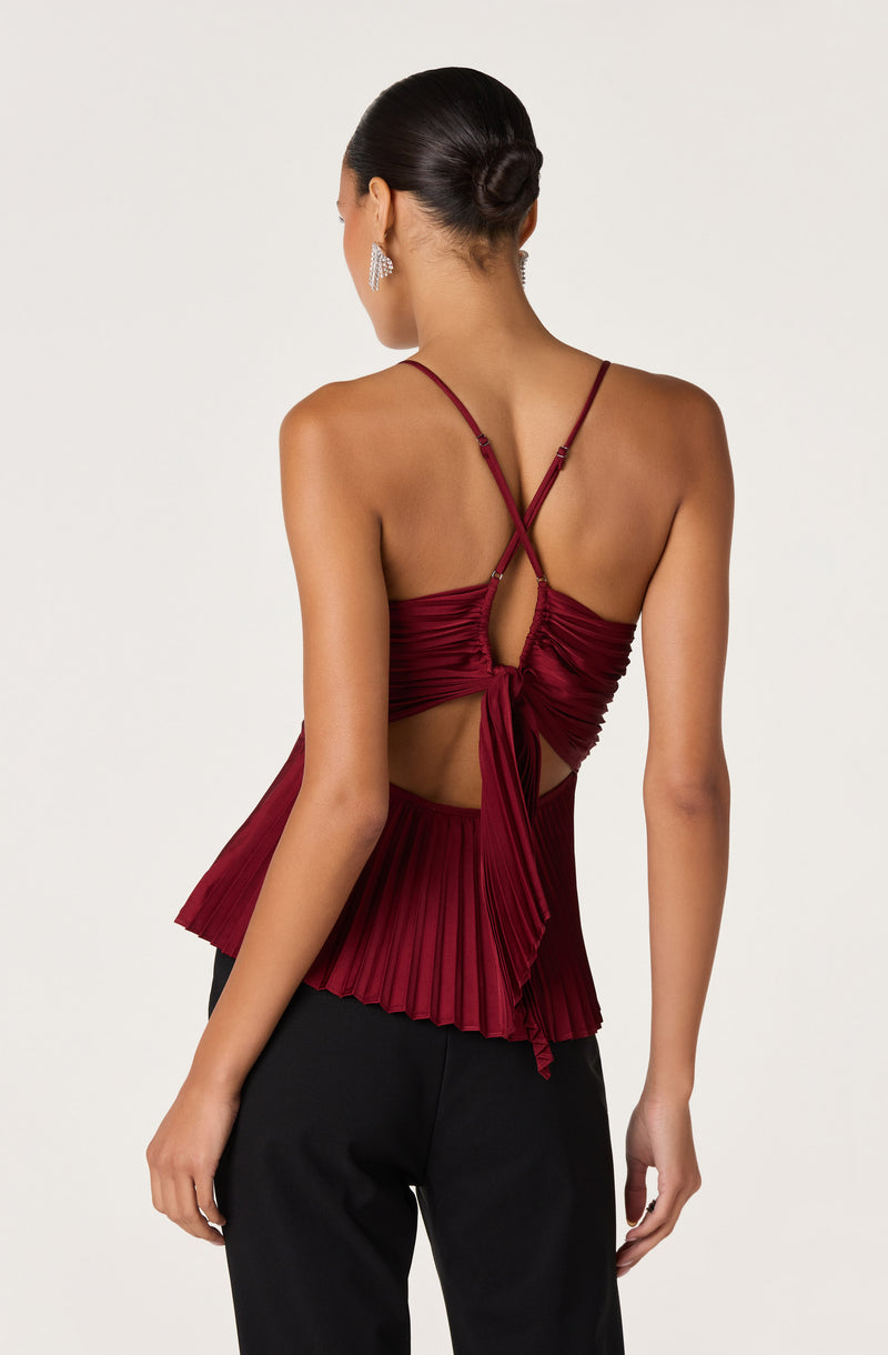 Woman wearing a burgundy pleated top with thin straps and a bow at the back.