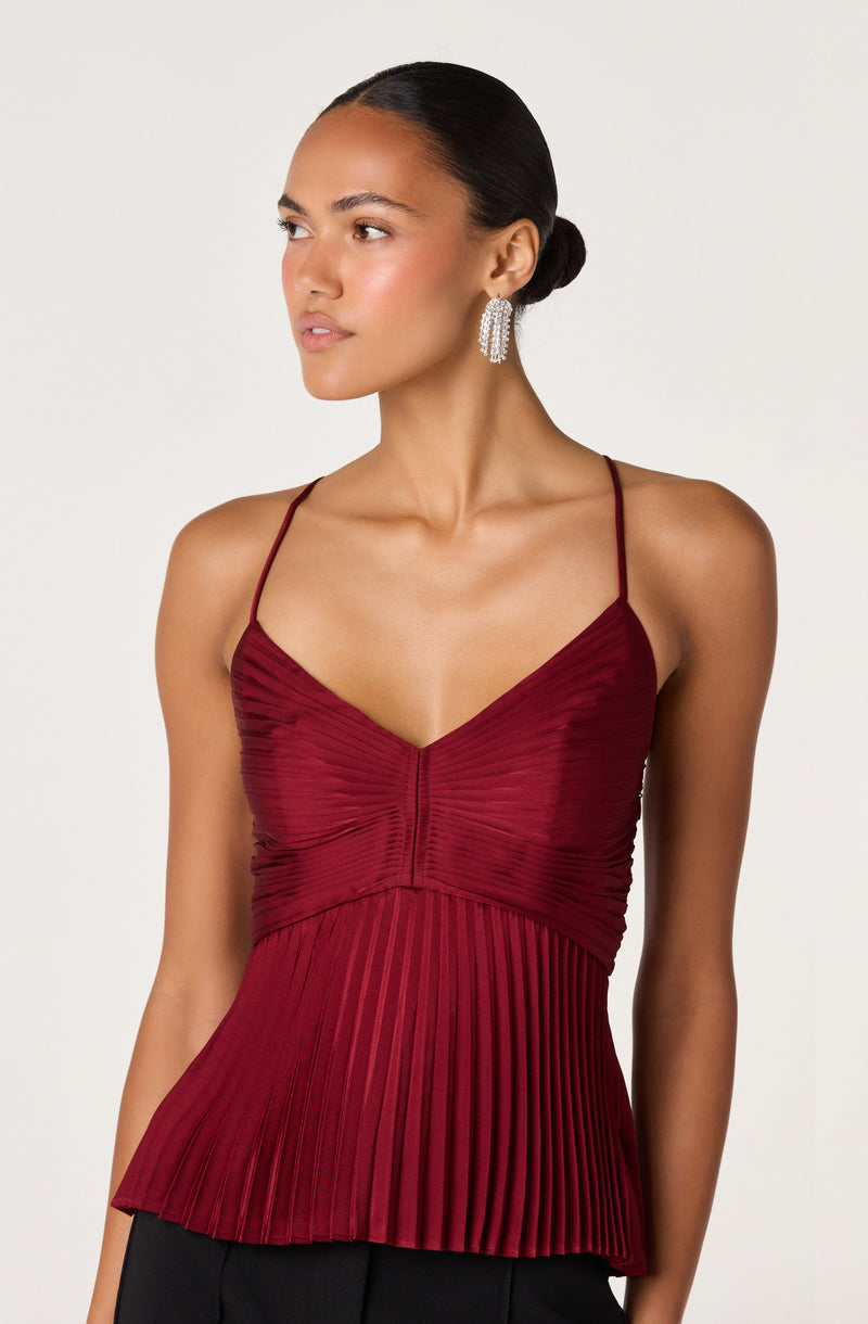 Woman wearing a red pleated sleeveless top with thin spaghetti straps.