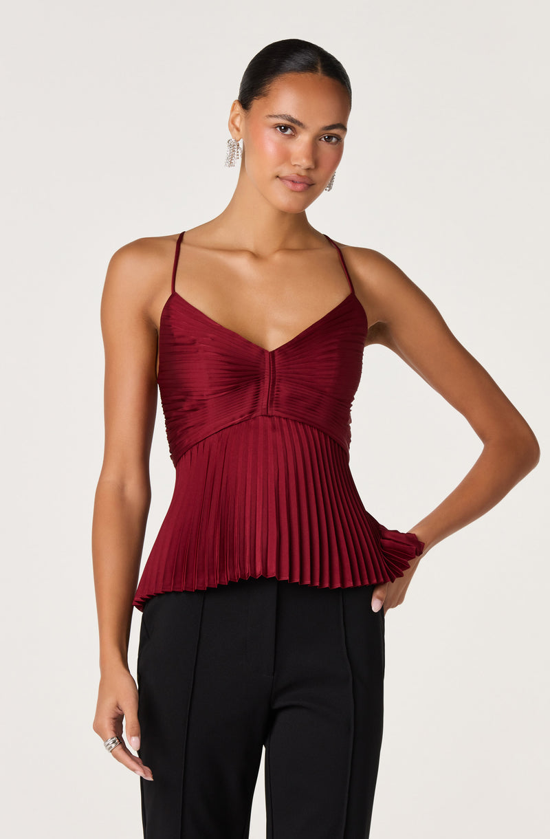 Woman in a red pleated spaghetti strap top with a V-neck, paired with black pants.