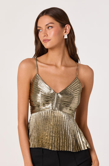 A young woman is wearing a metallic gold, pleated, sleeveless top with thin spaghetti straps. The top features a central zipper detail and has a slightly flared, ruffled hem. She is paired with black bottoms and accessorized with large, white, geometric-shaped earrings.